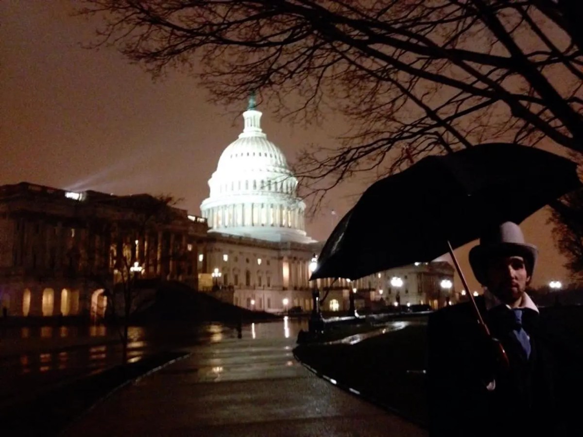 Person with umbrella near illuminated Capitol building at night.