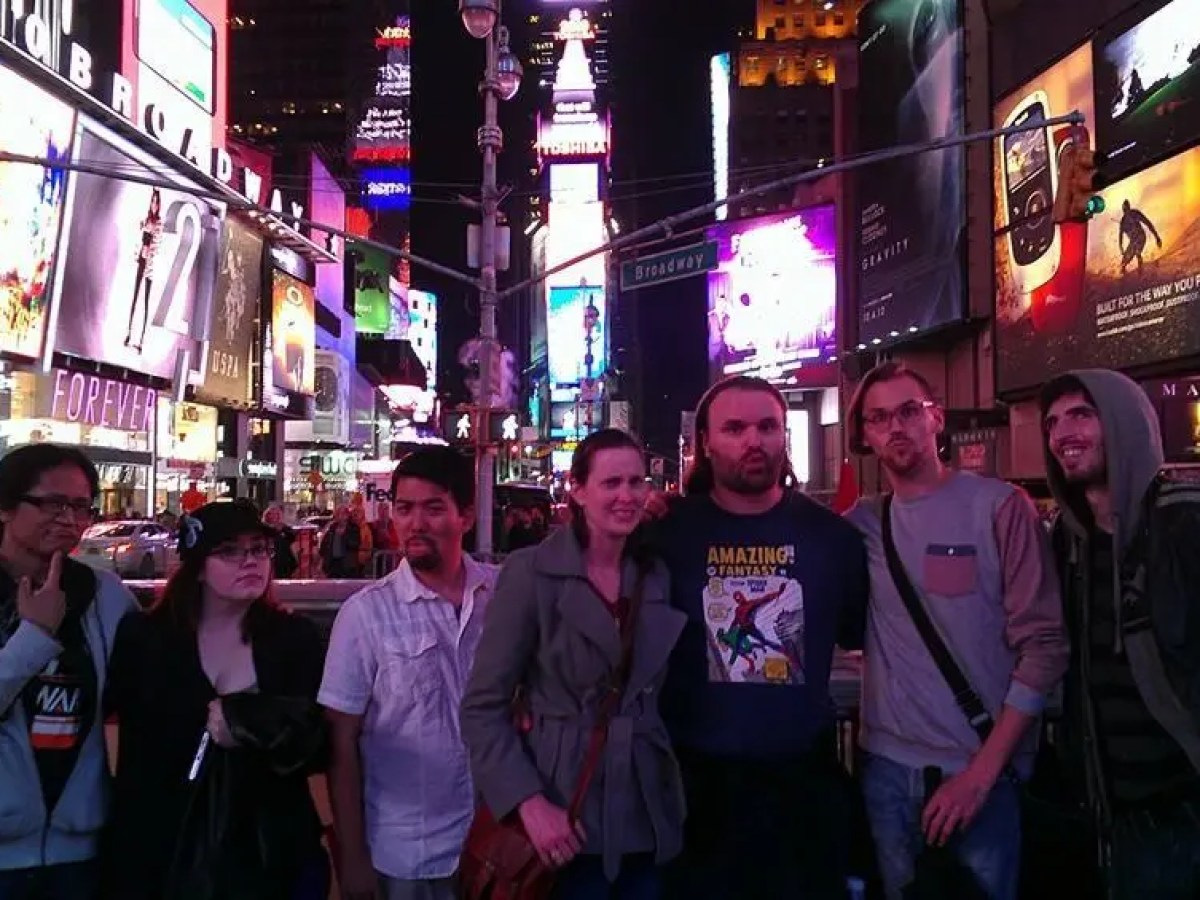 Group of people in Times Square at night, surrounded by bright billboards.