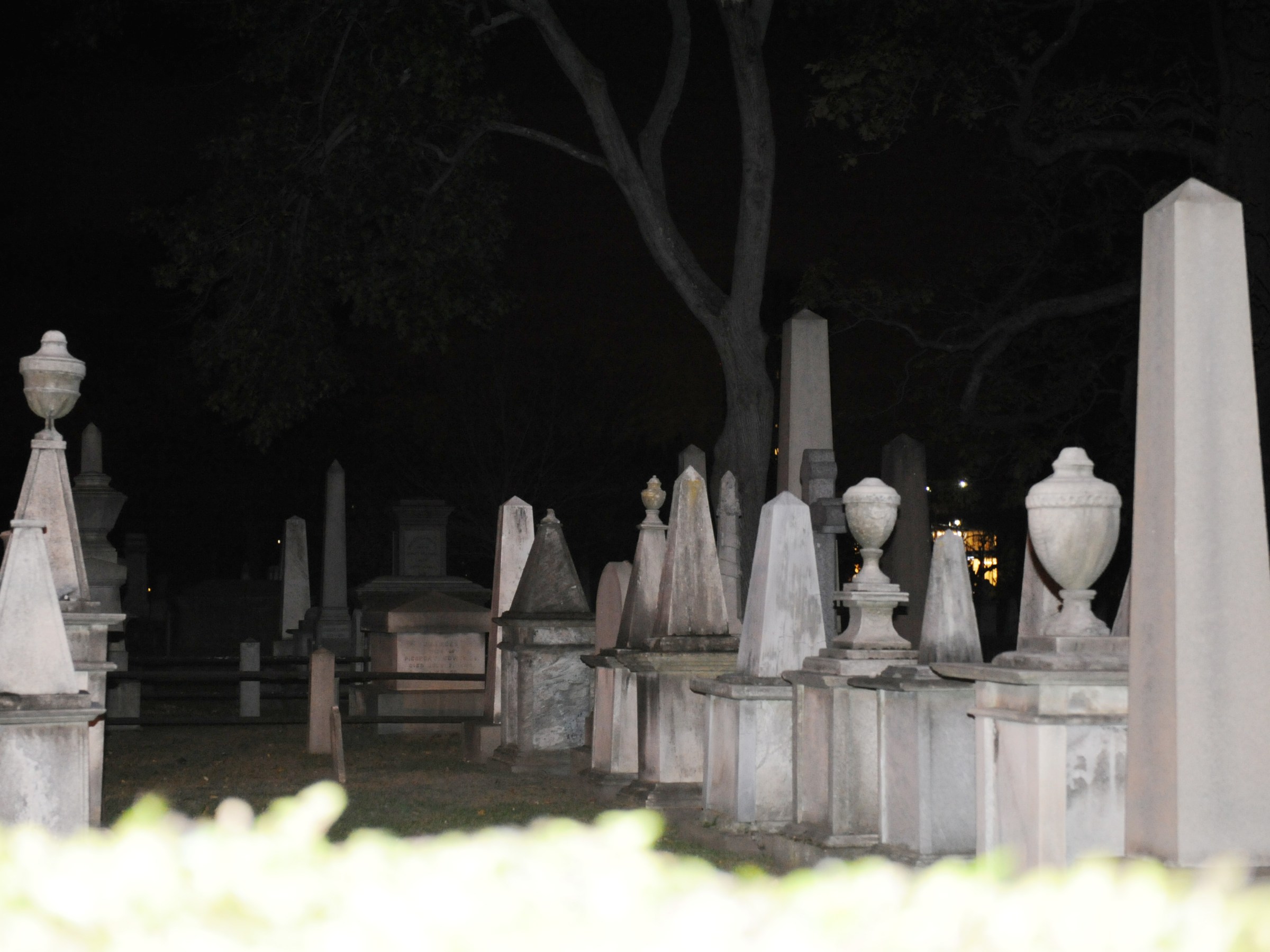 Cemetery at night with various tombstones and urn-shaped monuments.