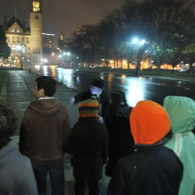 People in coats gathered on a wet night near a lit clock tower.