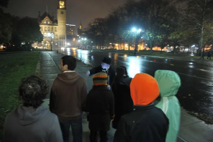 People in coats gathered on a wet night near a lit clock tower.