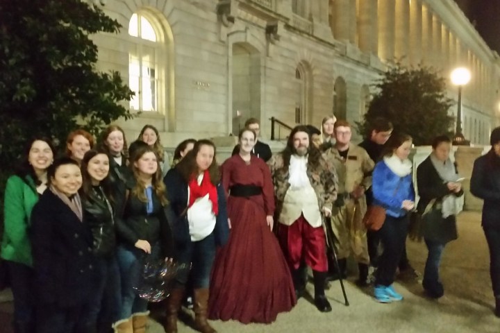 Group of people in various costumes posing outside a building at night.