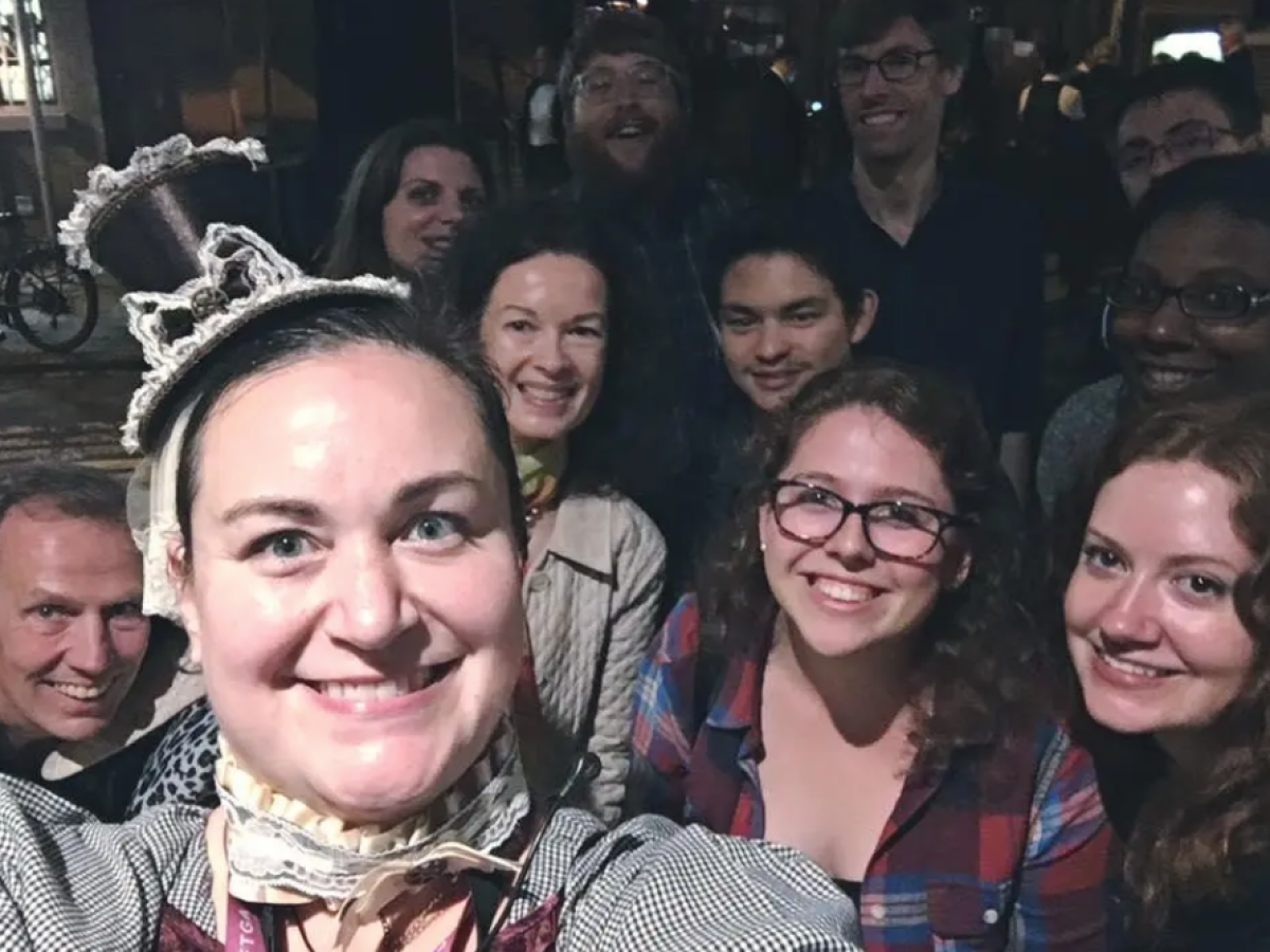 Group selfie with smiling people; woman in front wears a decorative headpiece.