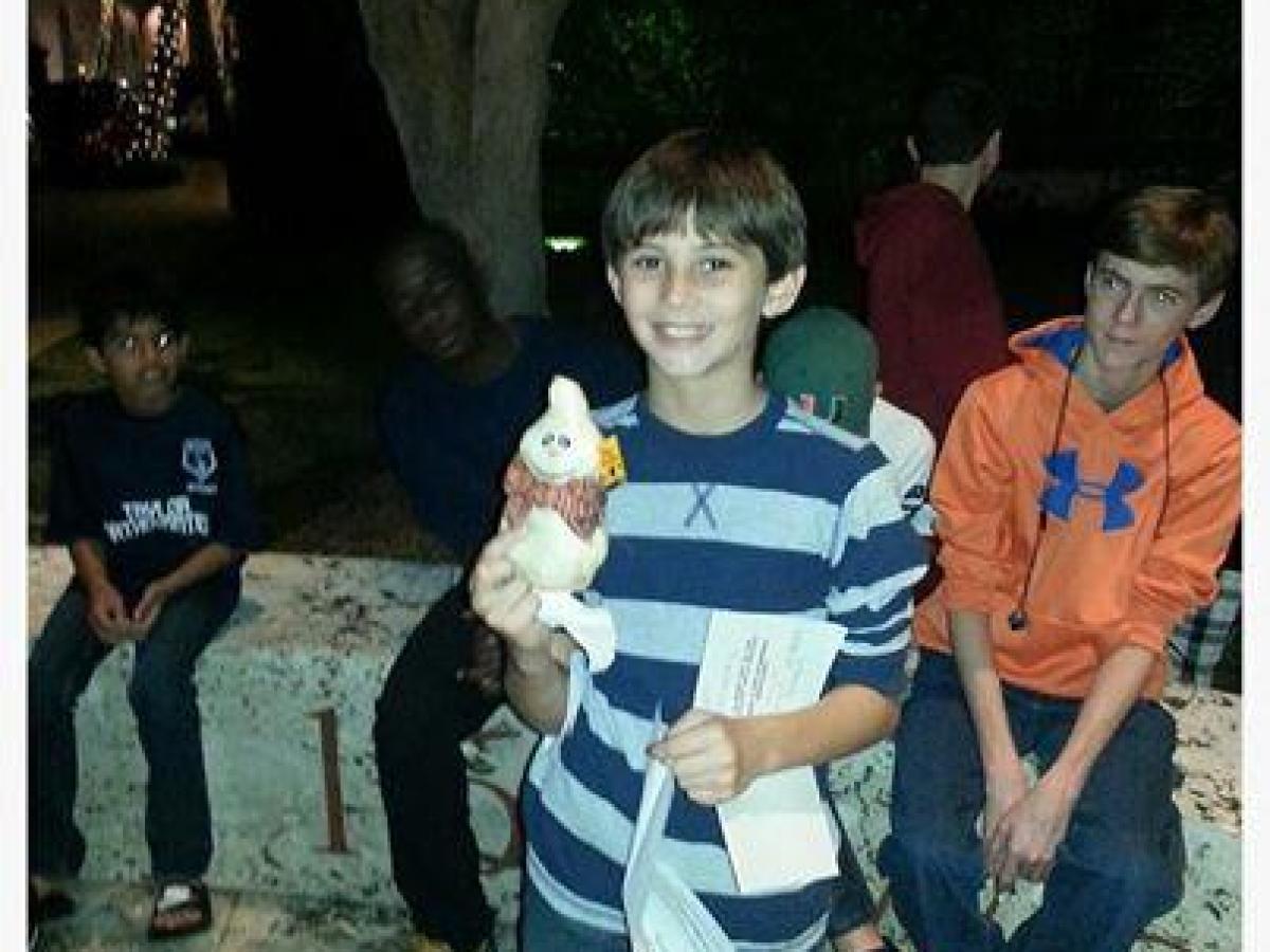 Group of kids seated outside with one holding a small white plushie, surrounded by text about a birthday message.