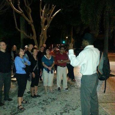 Person speaking to a group outdoors at night with trees in the background.