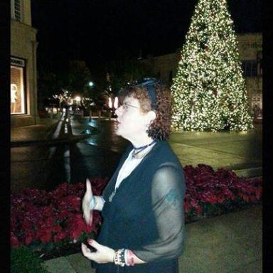 Woman speaking at night with a large lit Christmas tree and festive decorations in the background.