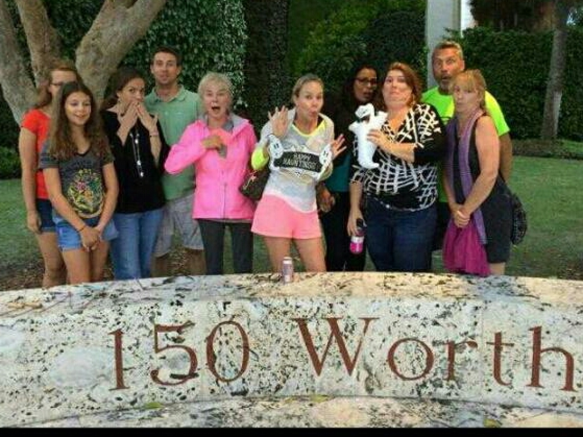 Group of people posing behind a stone sign reading '150 Worth'.