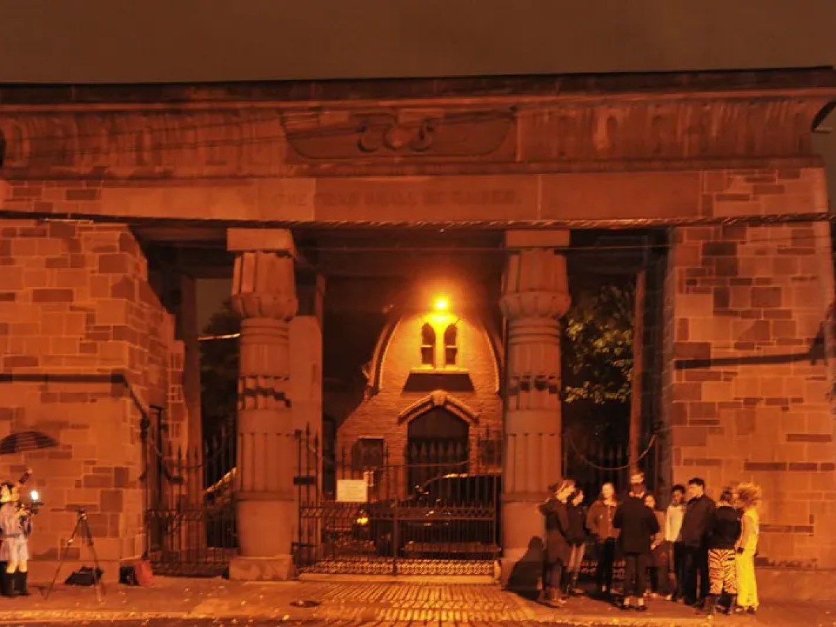 Group of people gathering under a large stone archway at night.