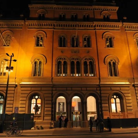 Illuminated historic building facade at night with arched windows and street lamps.