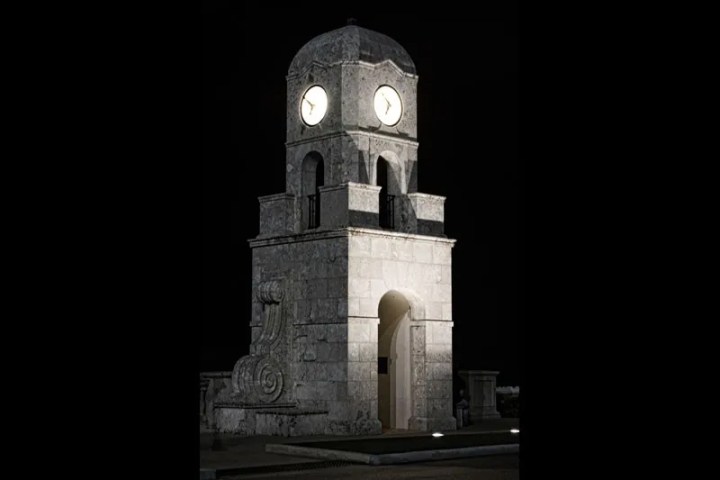 Illuminated stone clock tower with two clocks at night.