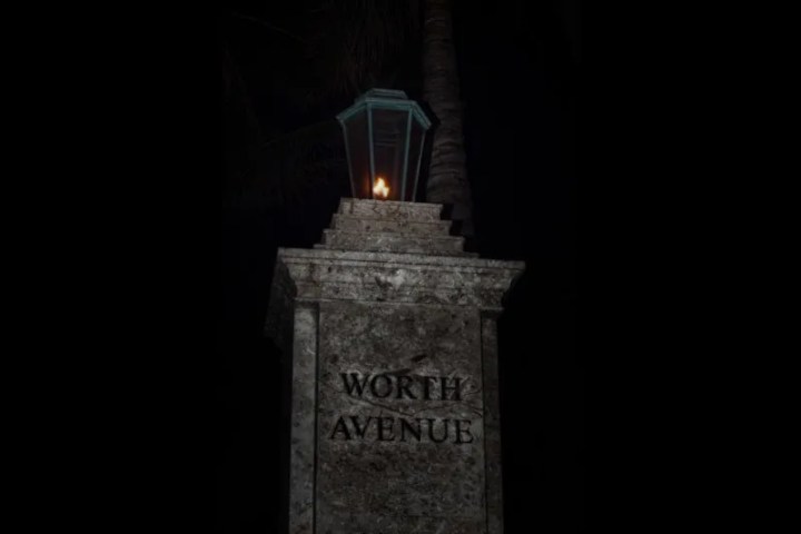 Stone pillar with 'WORTH AVENUE' and a lit lantern on top at night.
